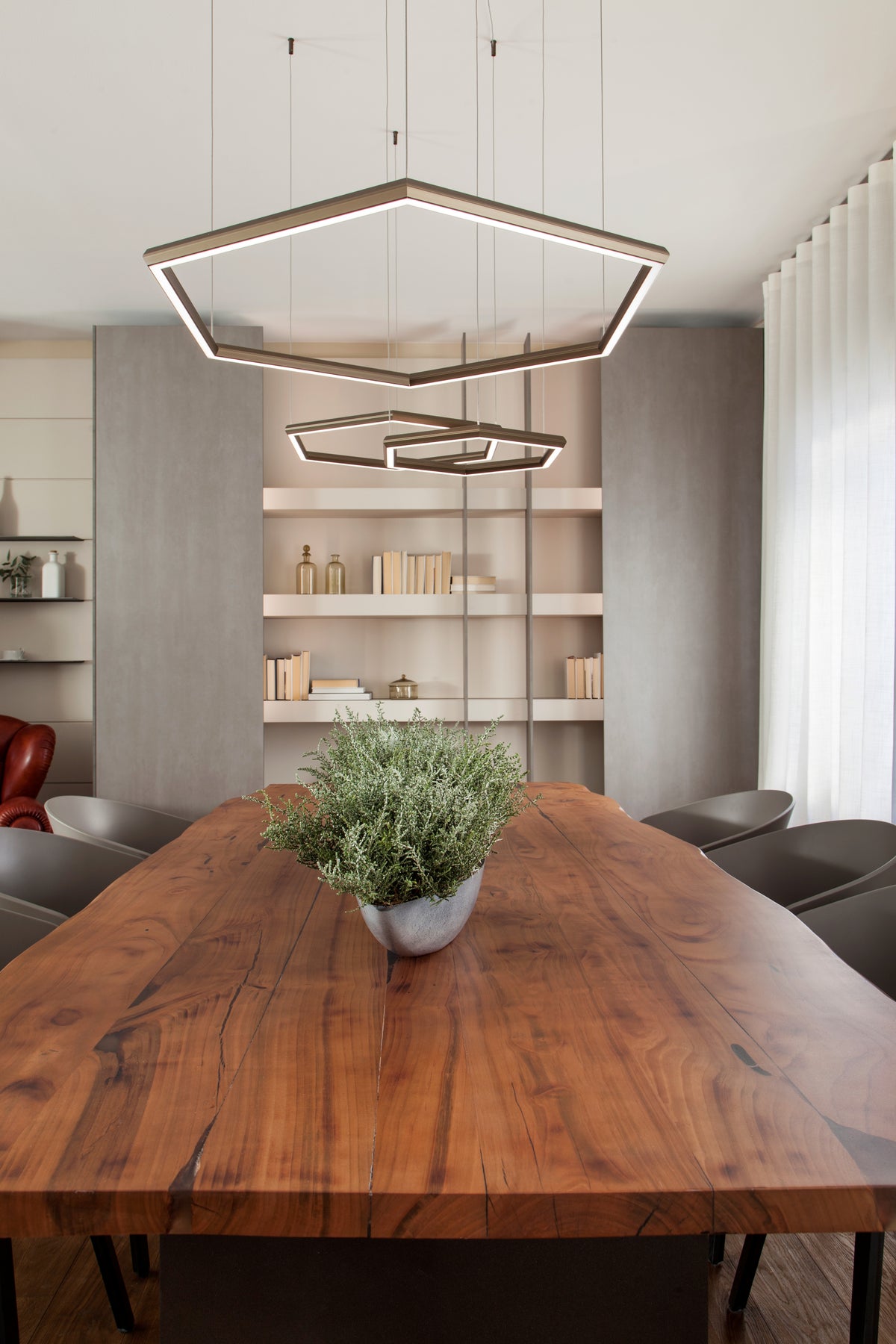 Dettaglio del tavolo da pranzo in legno massello con sospensioni geometriche e libreria a parete sullo sfondo