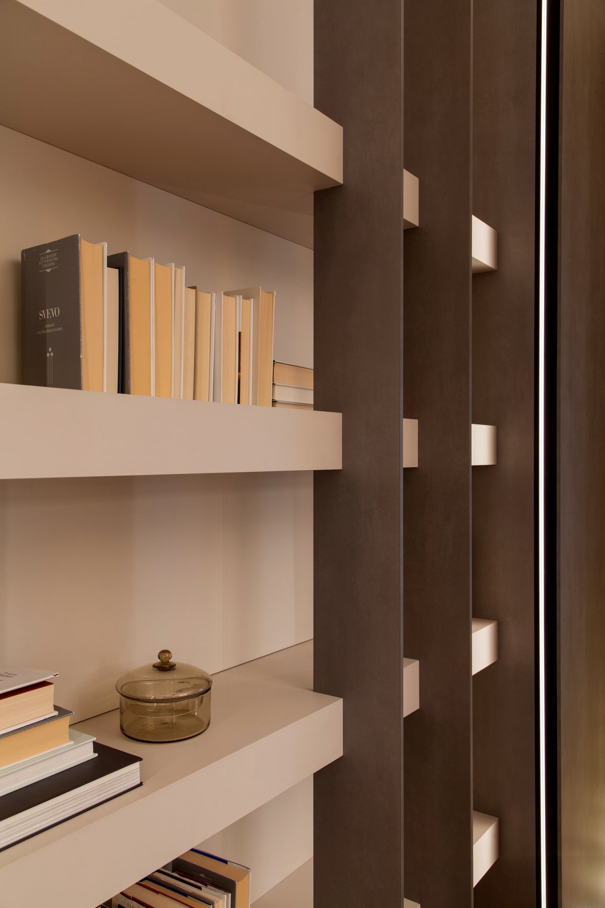 Dettaglio della libreria con mensole chiare, setti verticali scuri e illuminazione integrata