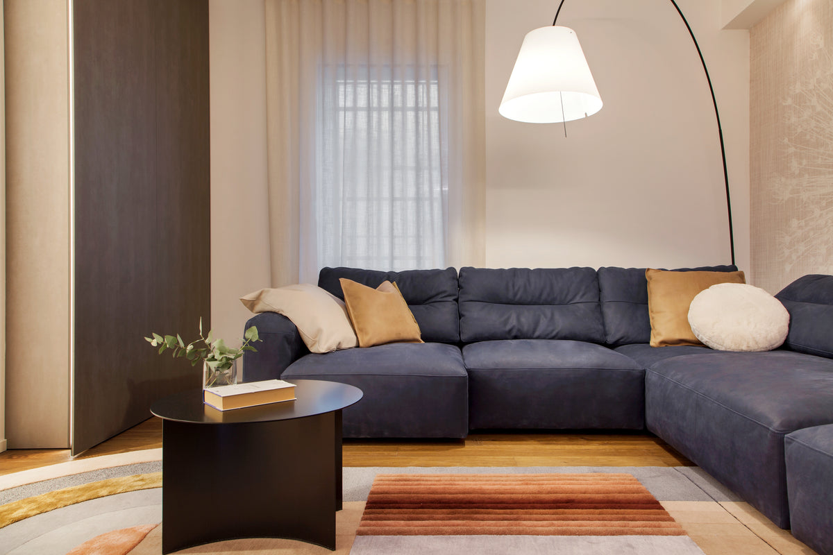 Living con divano blu, lampada ad arco e tappeto grafico, arredato con scelte ricercate e arredi contemporanei