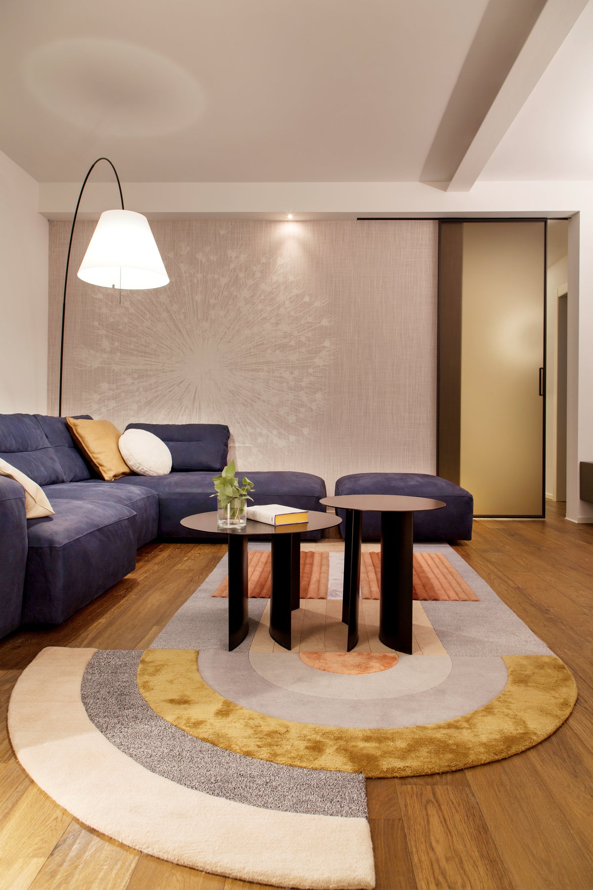 Zona relax con divano angolare blu, tavolini neri e parete decorativa con carta da parati, tappeto di design con forma irregolare