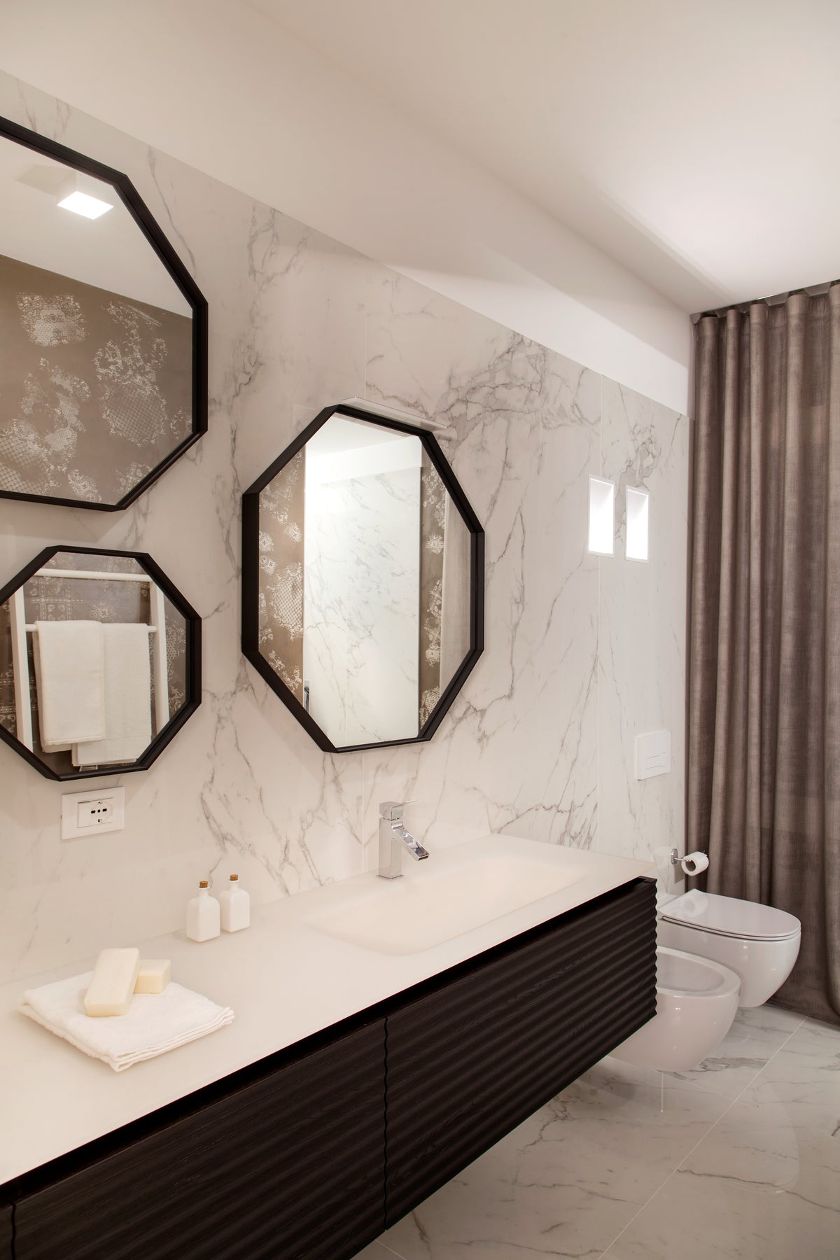 Bagno con rivestimento effetto marmo, mobile lavabo scuro con ante lavorate e specchi sagomati in un progetto di interior design su misura