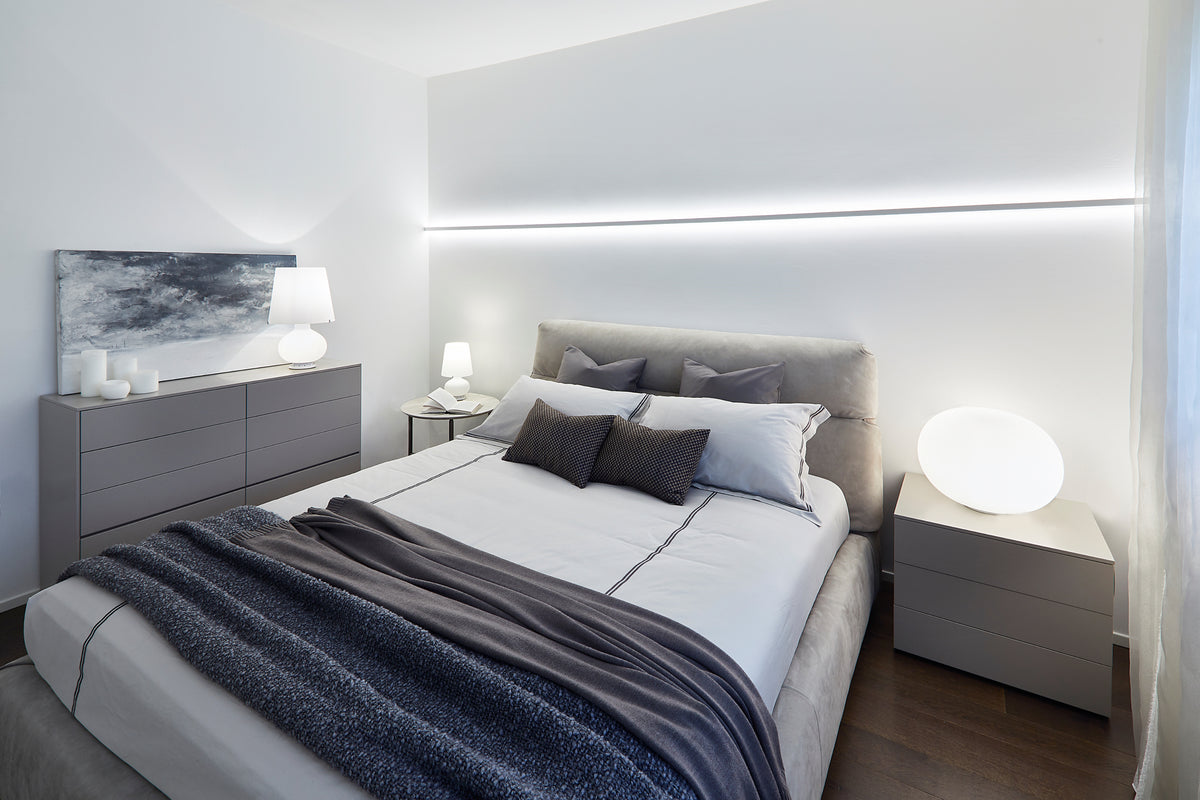 Camera matrimoniale contemporanea con letto imbottito in pelle, arredi coordinati e illuminazione lineare integrata a parete