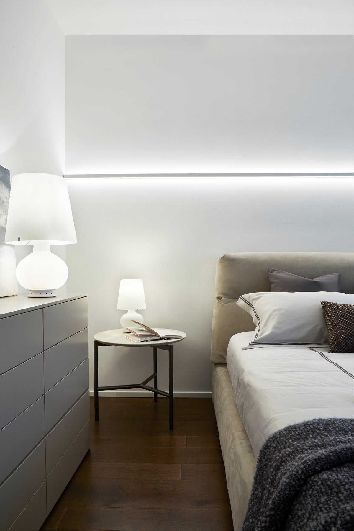 Dettaglio della camera padronale con letto a testiera imbottita, comodino minimale in pietra e luce integrata a parete, con arredo su misura per zona notte