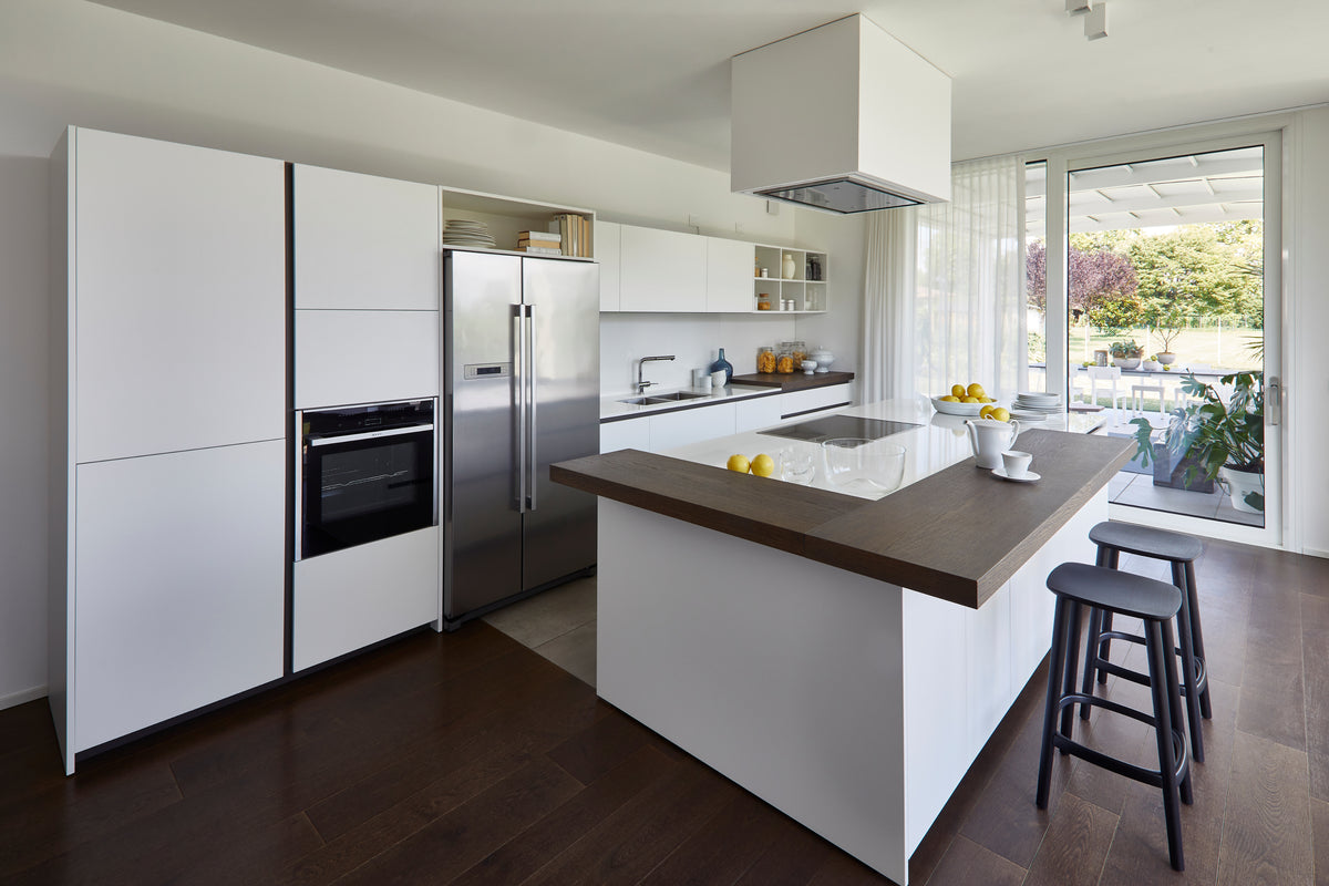 Cucina moderna con isola centrale e finiture bianche e legno, in spazio open space luminoso per la convivialità quotidiana