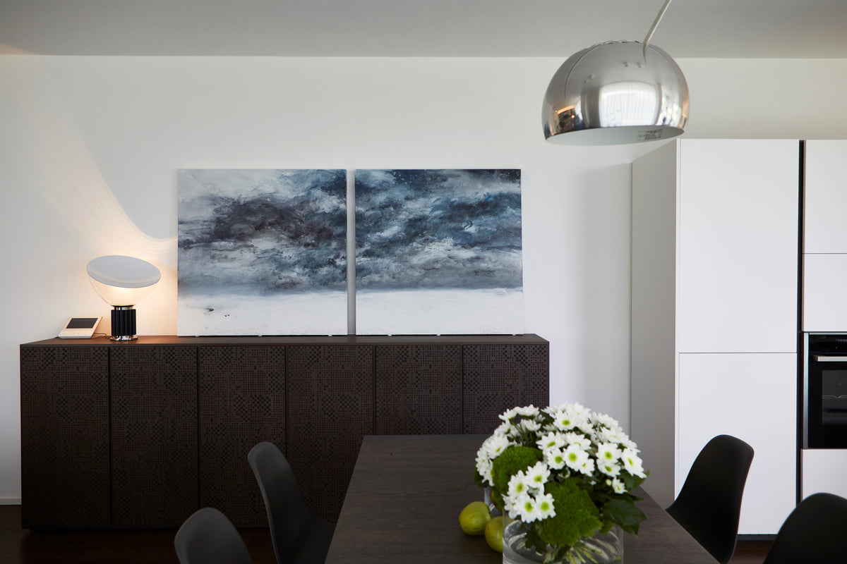 Zona pranzo con tavolo scuro, madia in legno con ante lavorate, lampada di design e opera astratta