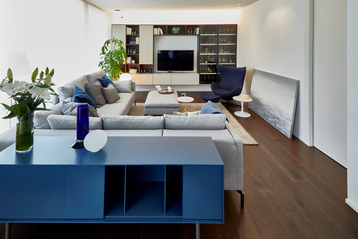 Living contemporaneo con grande divano modulare, madia retro divano colorata, tappeto chiaro e libreria integrata con TV