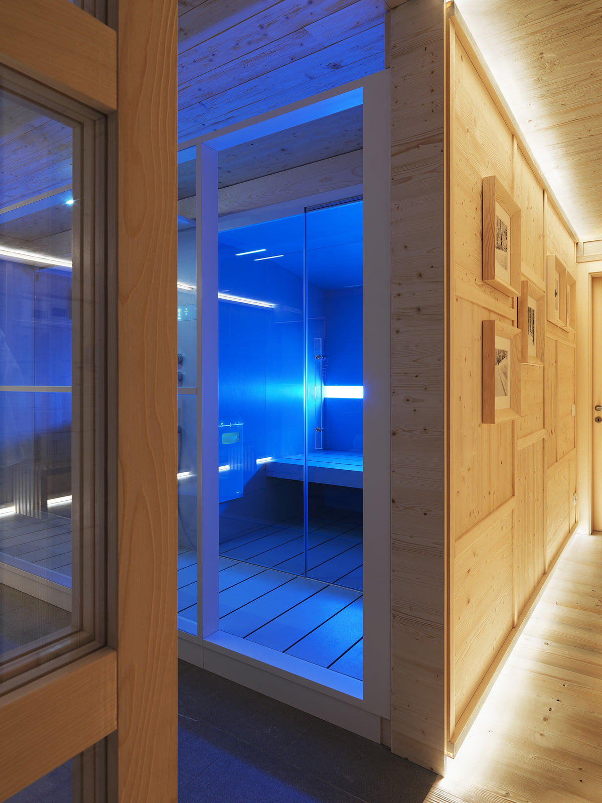 Corridoio in legno con vetrata sulla home spa illuminata, connessione tra zona notte e area wellness