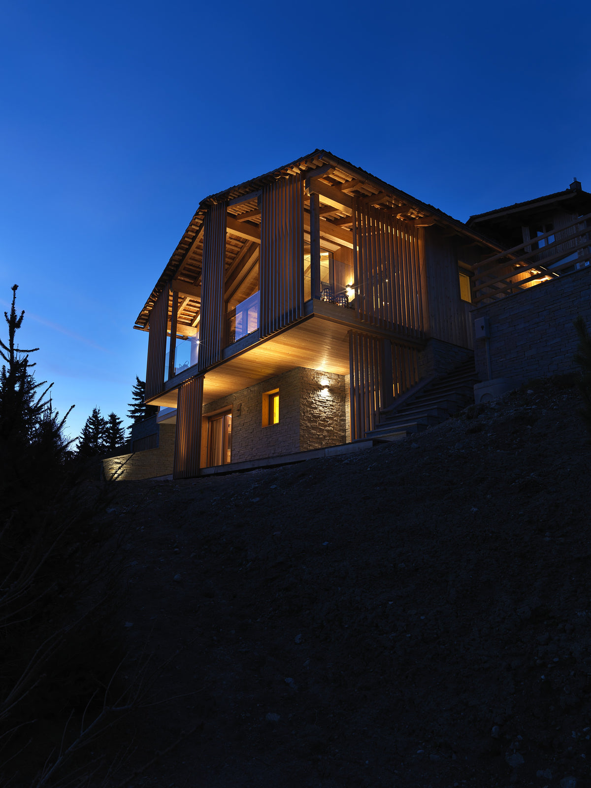 Prospetto della casa in legno e pietra con grandi vetrate e luce serale
