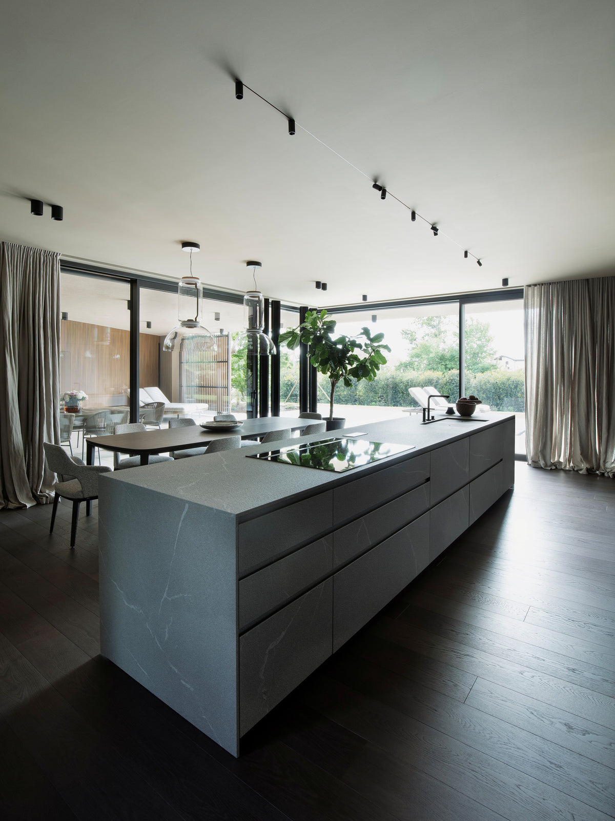 Cucina con grande isola in finitura pietra, zona pranzo e affaccio sulla piscina