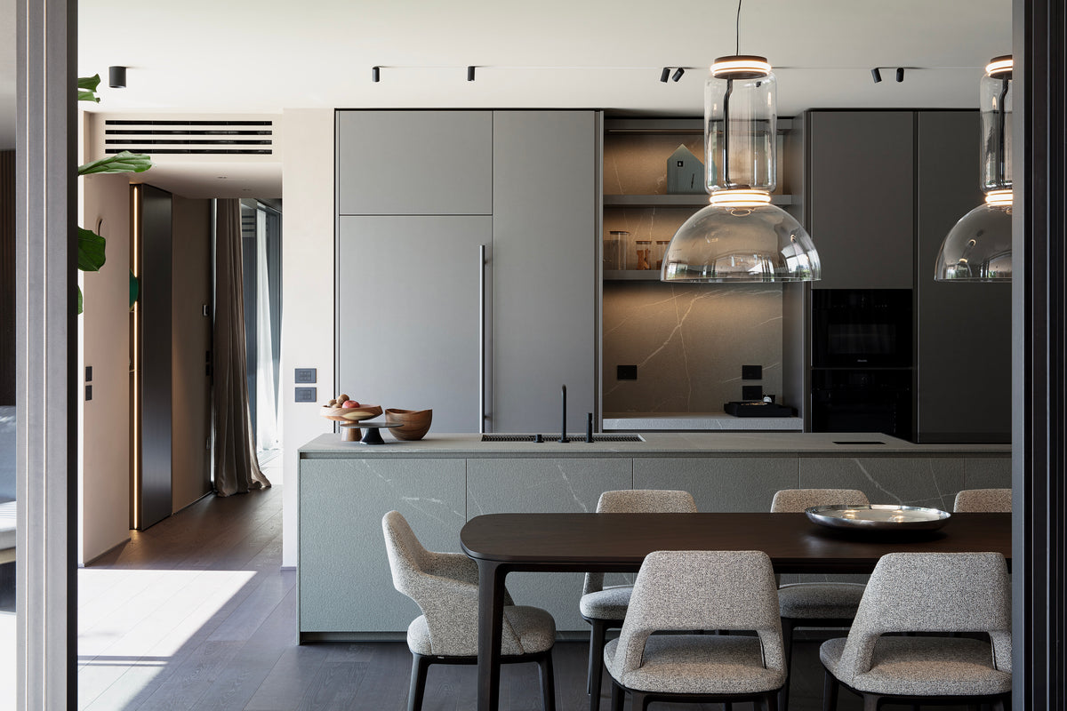 Cucina e dining con isola centrale, tavolo in legno e grandi sospensioni in vetro Flos