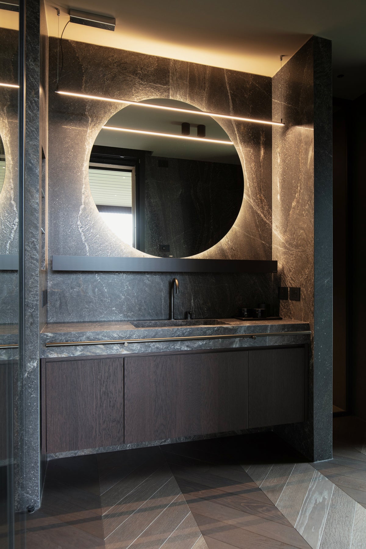 Bagno padronale con mobile lavabo in pietra scura e specchio rotondo retroilluminato