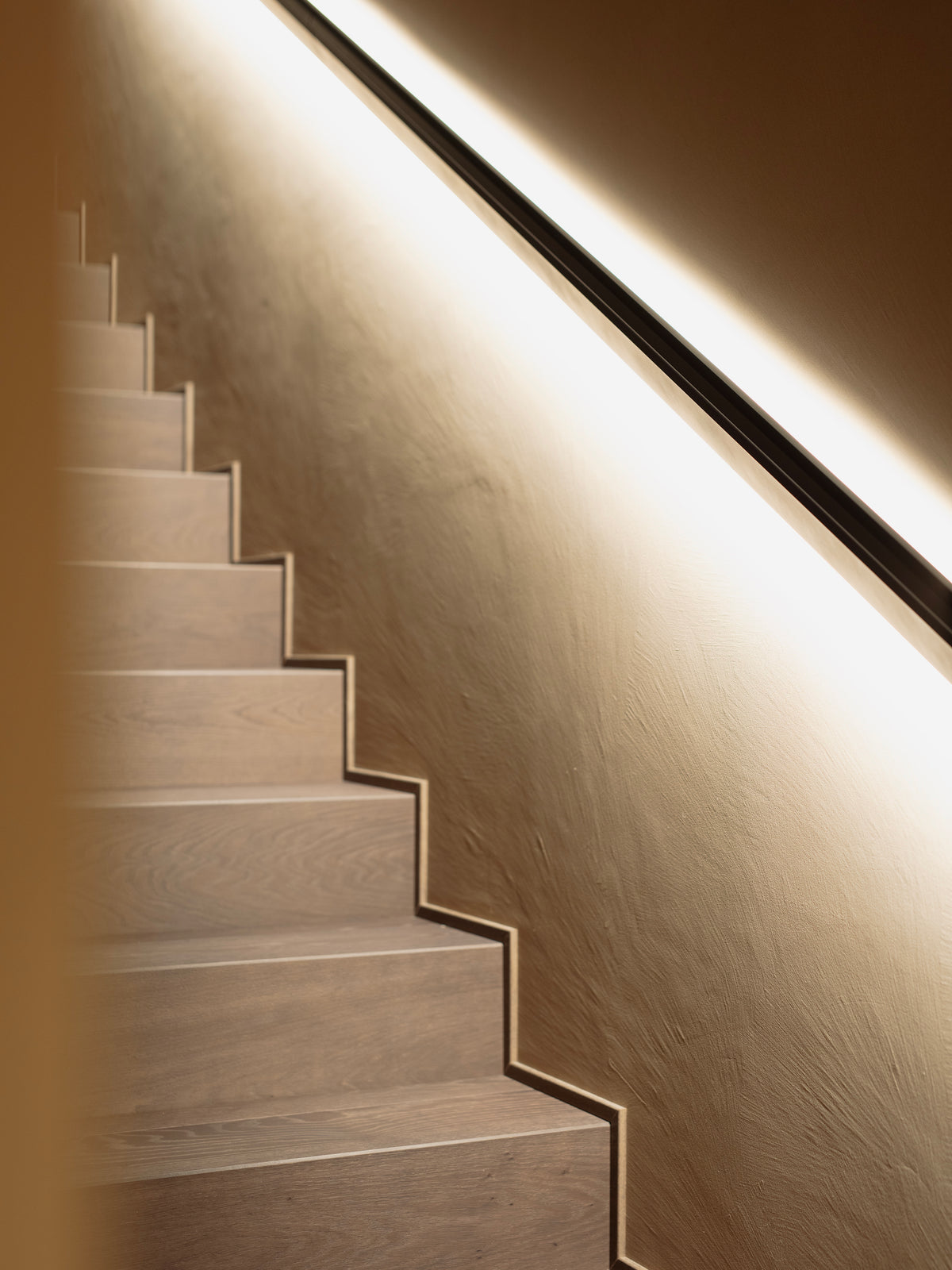 Scala interna con illuminazione lineare a parete e finiture materiche essenziali