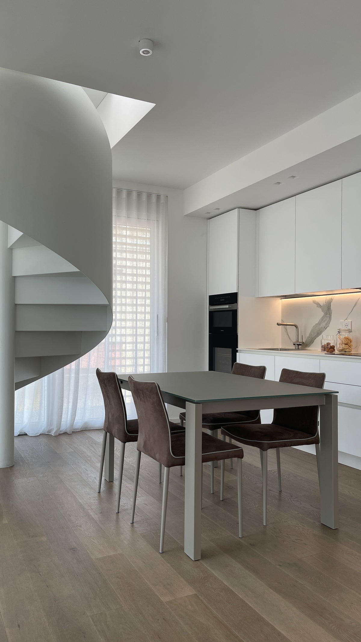 Interior design di attico di nuova costruzione sul Lago di Garda con cucina bianca, zona pranzo e scala a chiocciola