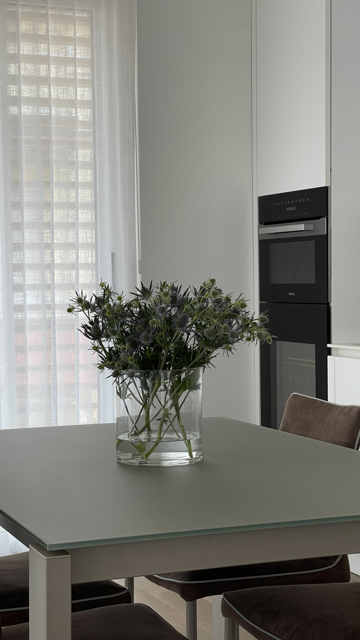 Tavolo da pranzo con composizione floreale e cucina bianca sullo sfondo