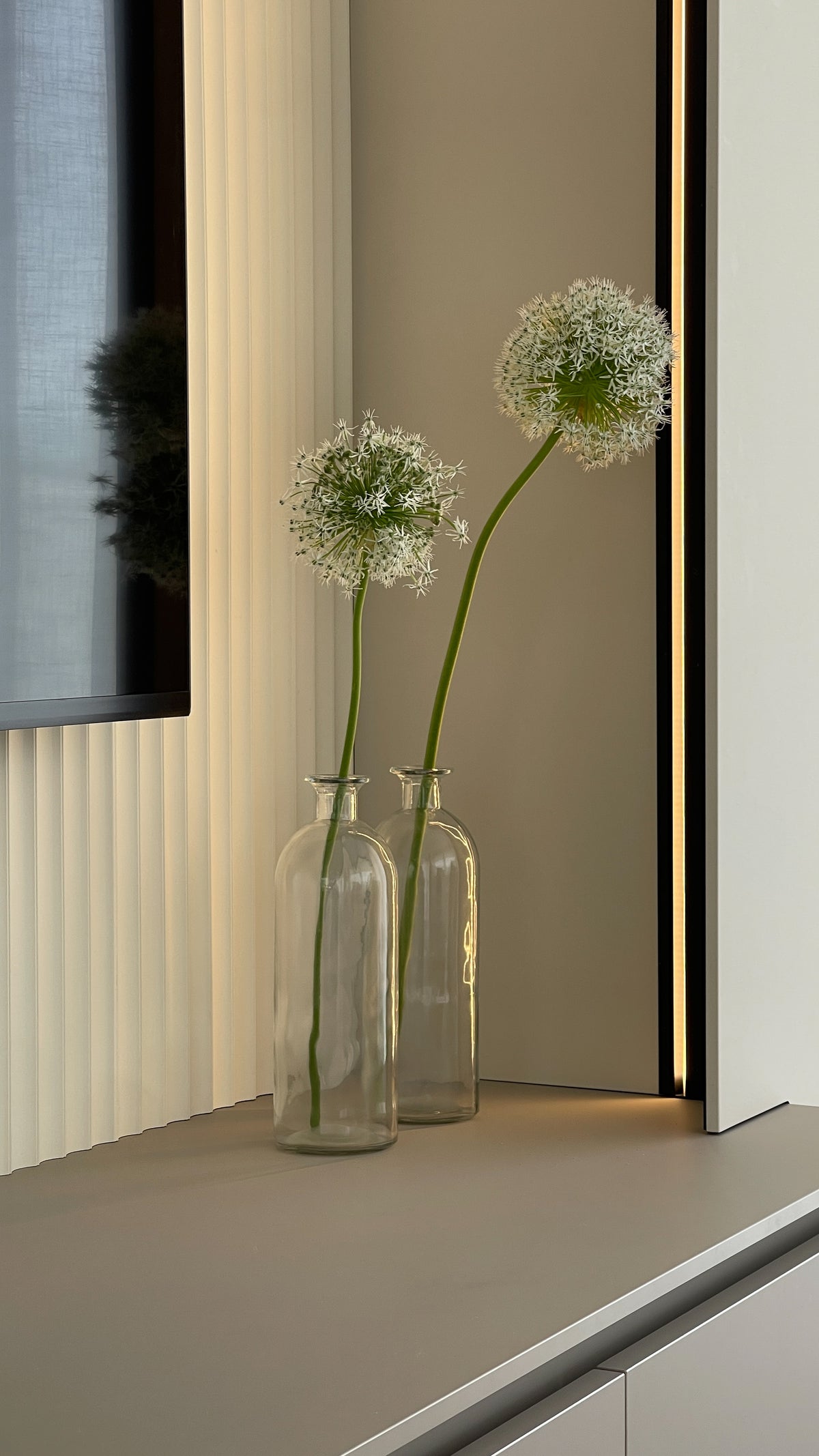 Dettaglio decorativo con vasi in vetro e illuminazione verticale integrata nella parete TV