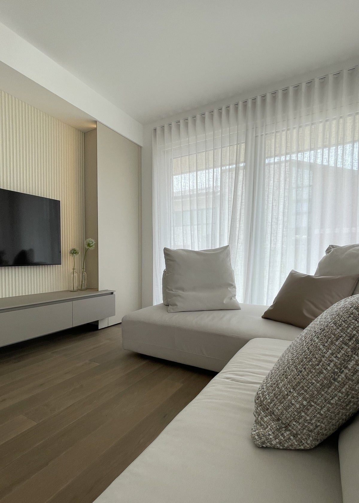 Living contemporaneo con divano modulare chiaro, parete TV su misura e pavimento in legno