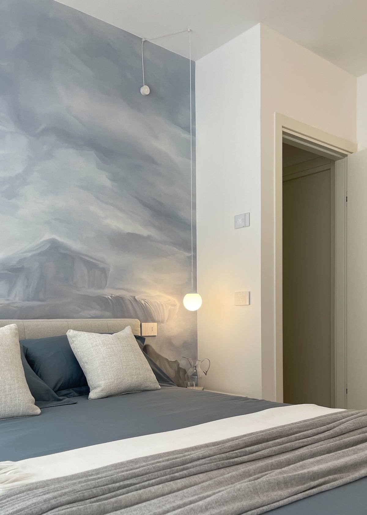 Camera da letto con parete decorativa panoramica, letto imbottito e palette nei toni chiari e azzurri