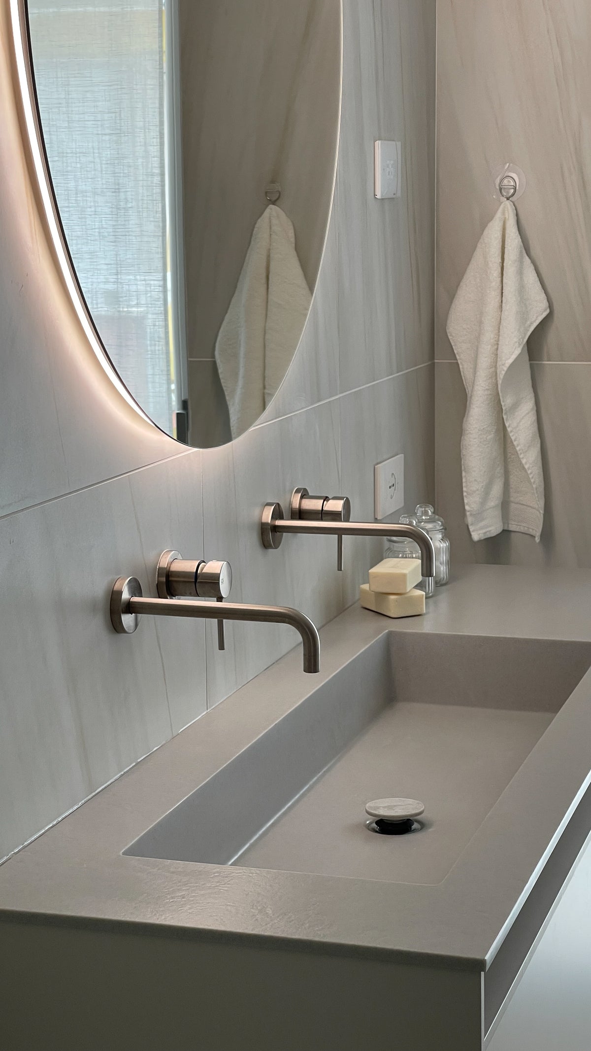 Dettaglio del lavabo integrato con rubinetteria a parete e specchio retroilluminato nel bagno contemporaneo