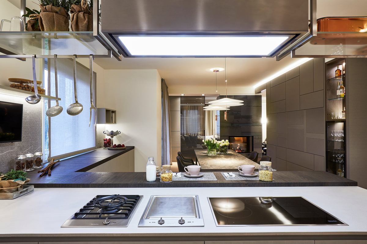 Cucina open space con piano cottura integrato, piastra in acciaio e piano snack con affaccio diretto sulla zona pranzo, progettazione per la convivialità
