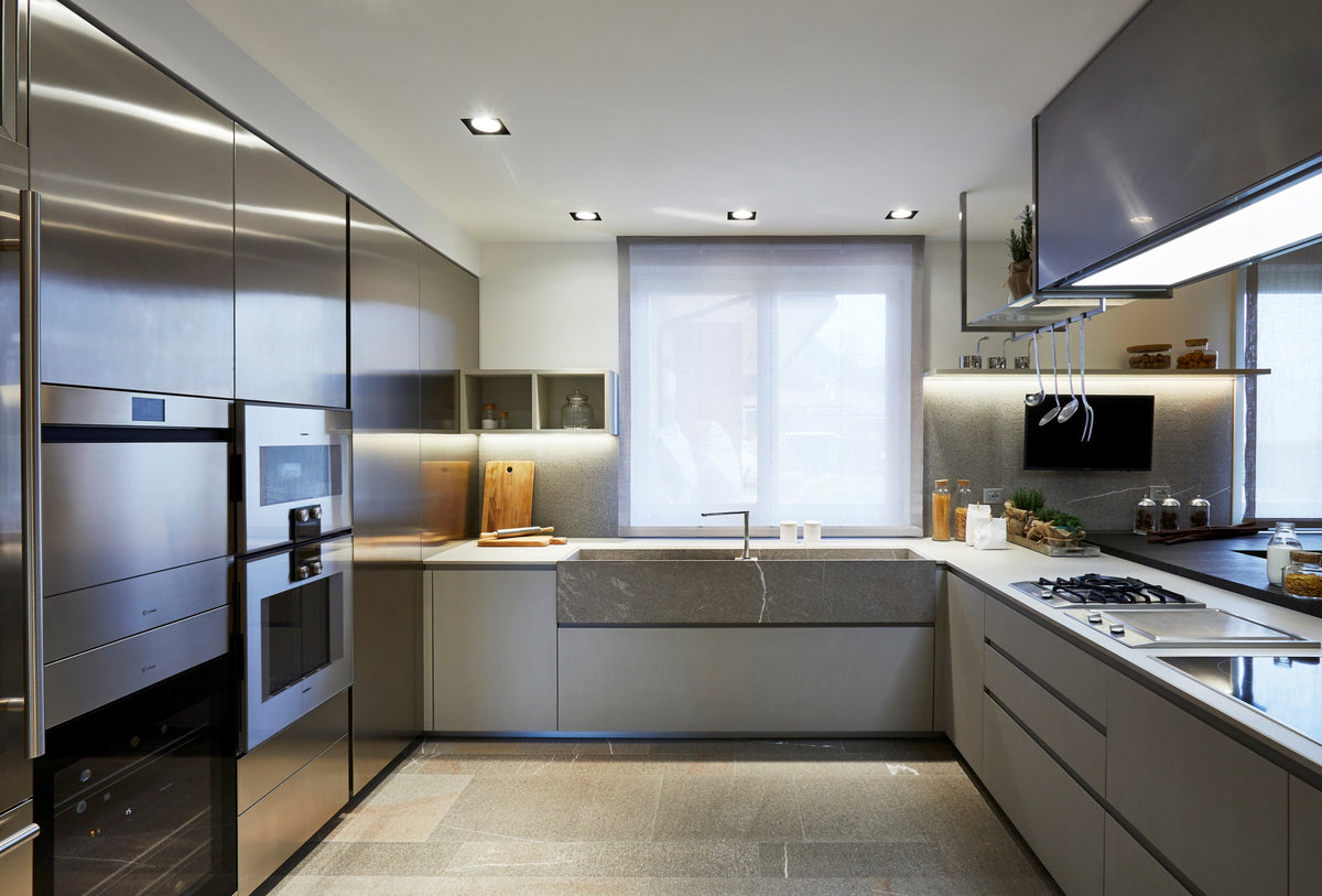 Cucina contemporanea con composizione a U e penisola con piano snack, elementi sospesi, arredi in acciaio inox e piano di lavoro in pietra