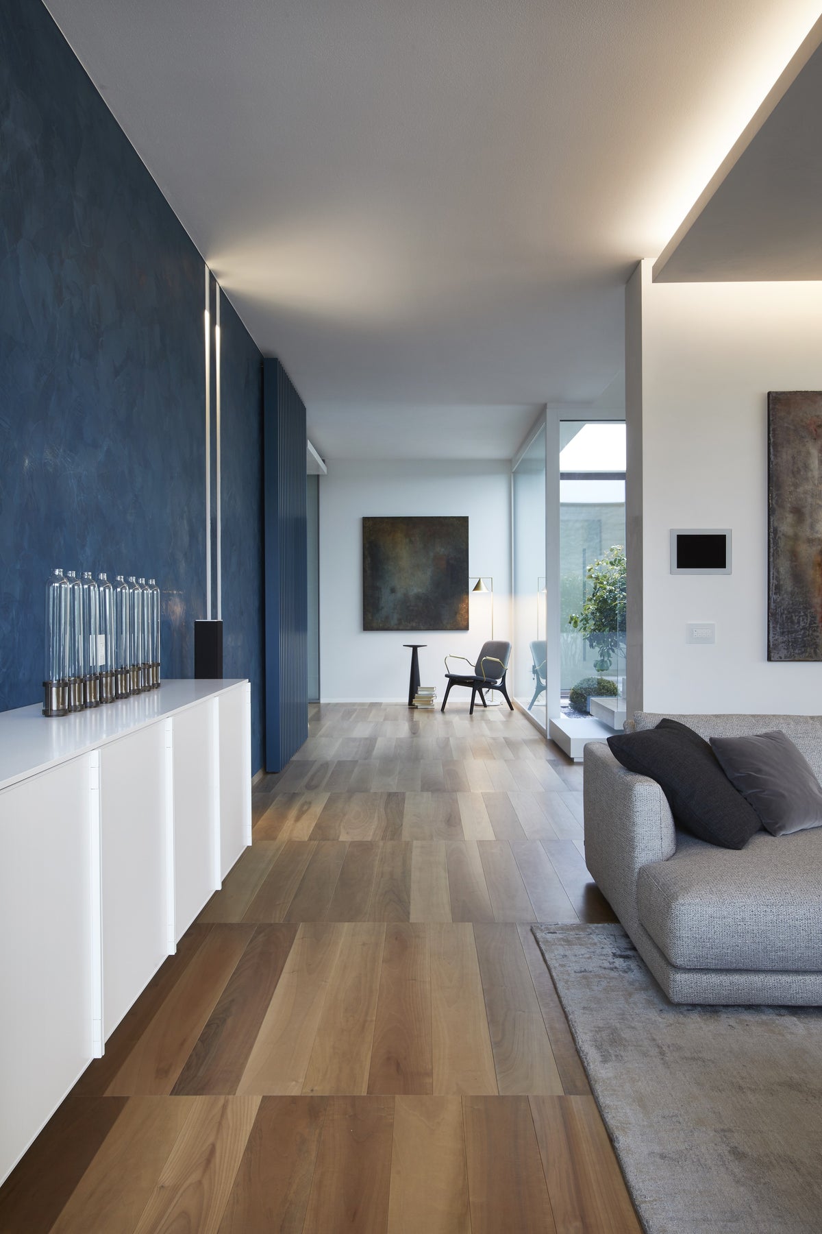 Corridoio della zona giorno con parete materica blu, luce naturale e passaggio fluido verso il living