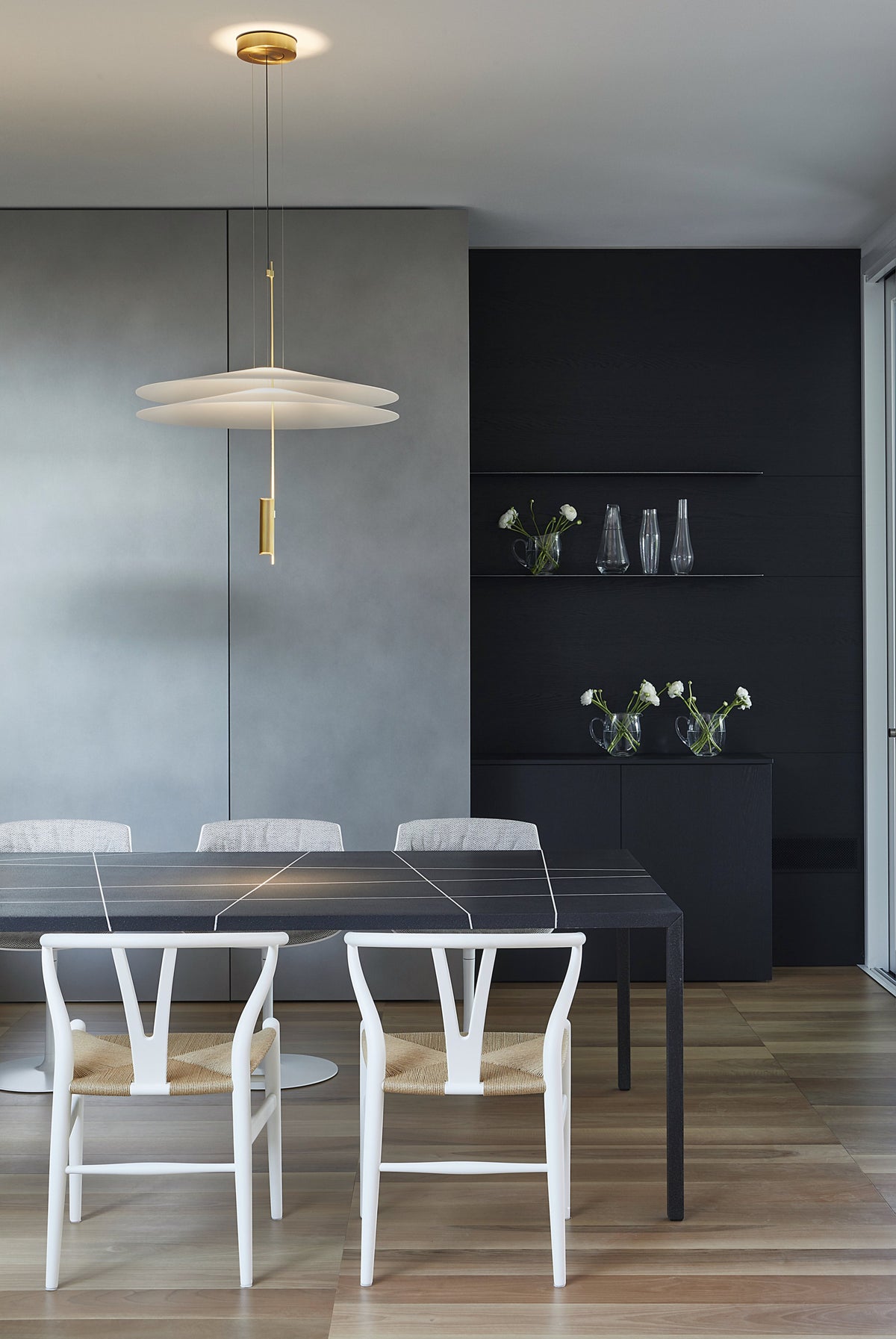 Zona pranzo con tavolo minimale, sedute di design Carl Hansen e parete attrezzata scura