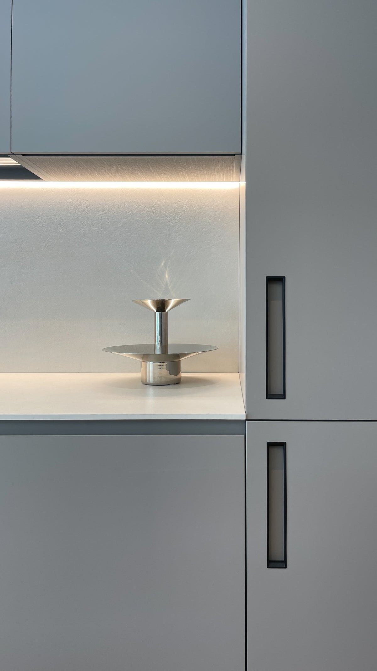 Dettaglio della cucina su misura con colonne a tutta altezza, illuminazione integrata e finiture neutre