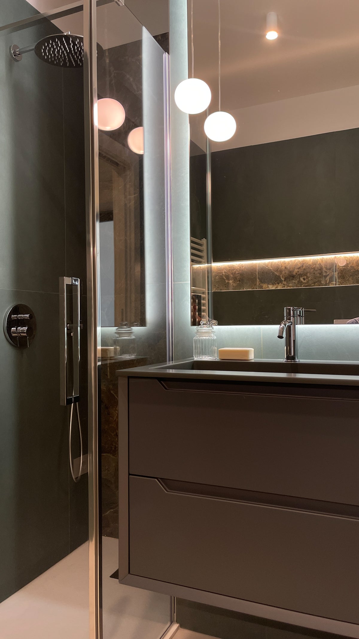 Bagno su misura con mobile sospeso, doccia in vetro, specchio illuminato e rivestimenti materici verde scuro