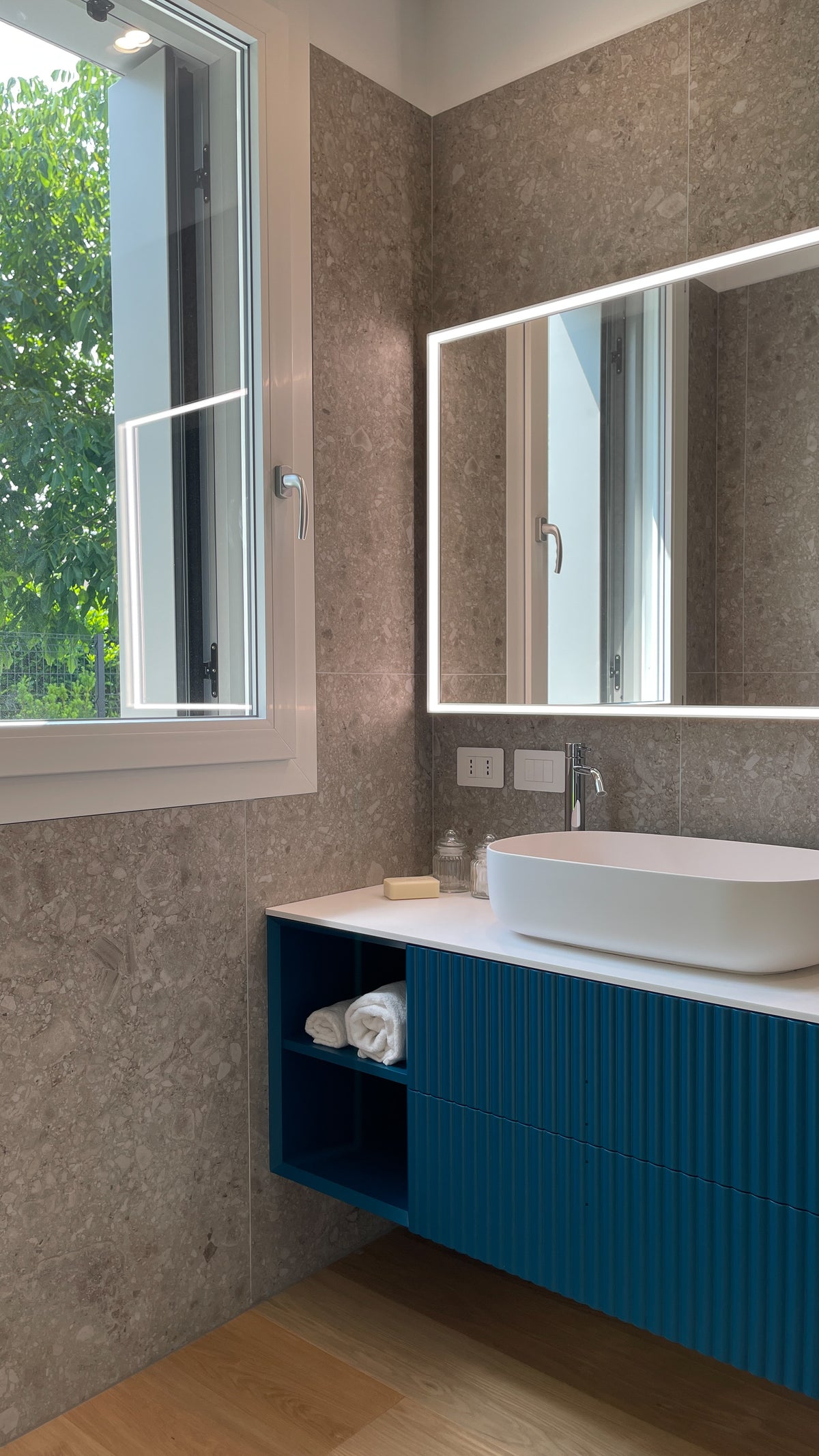 Mobile bagno su misura blu ottanio con frontali lavorati, lavabo da appoggio e rivestimento effetto ceppo di gré