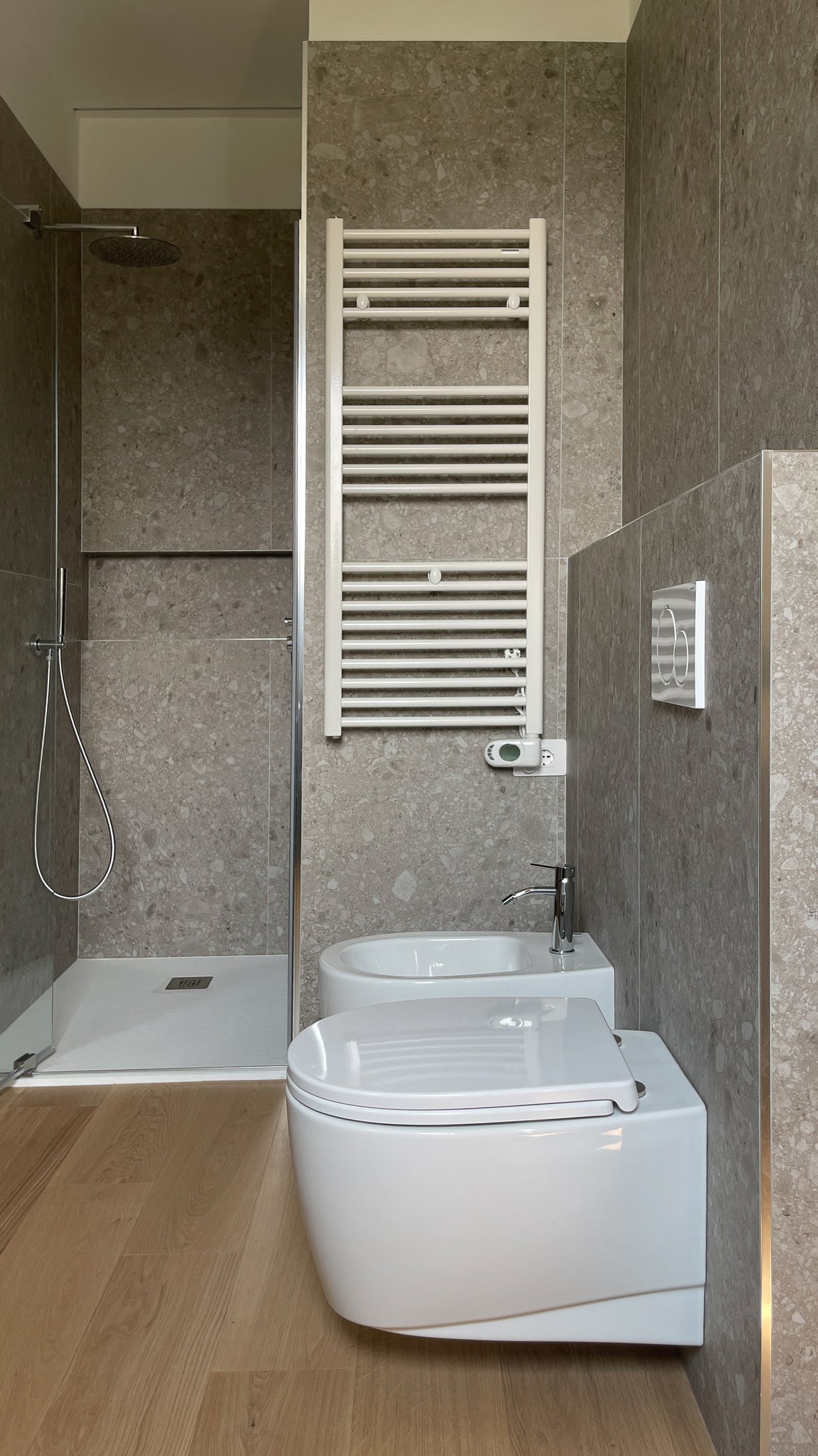 Bagno con doccia, sanitari sospesi e rivestimento continuo effetto ceppo di gré
