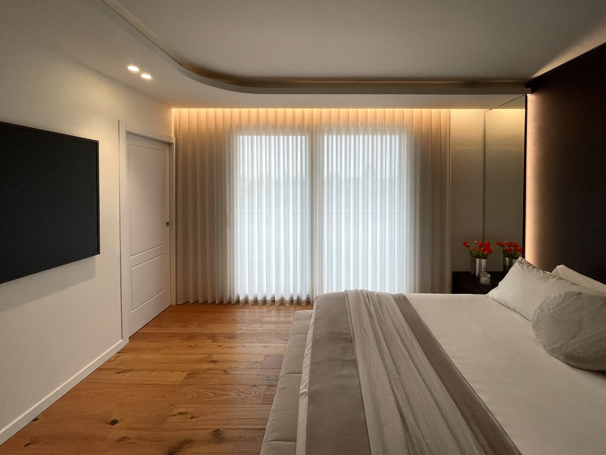 Vista della camera da letto con parete TV, pavimento in legno e illuminazione integrata nel controsoffitto