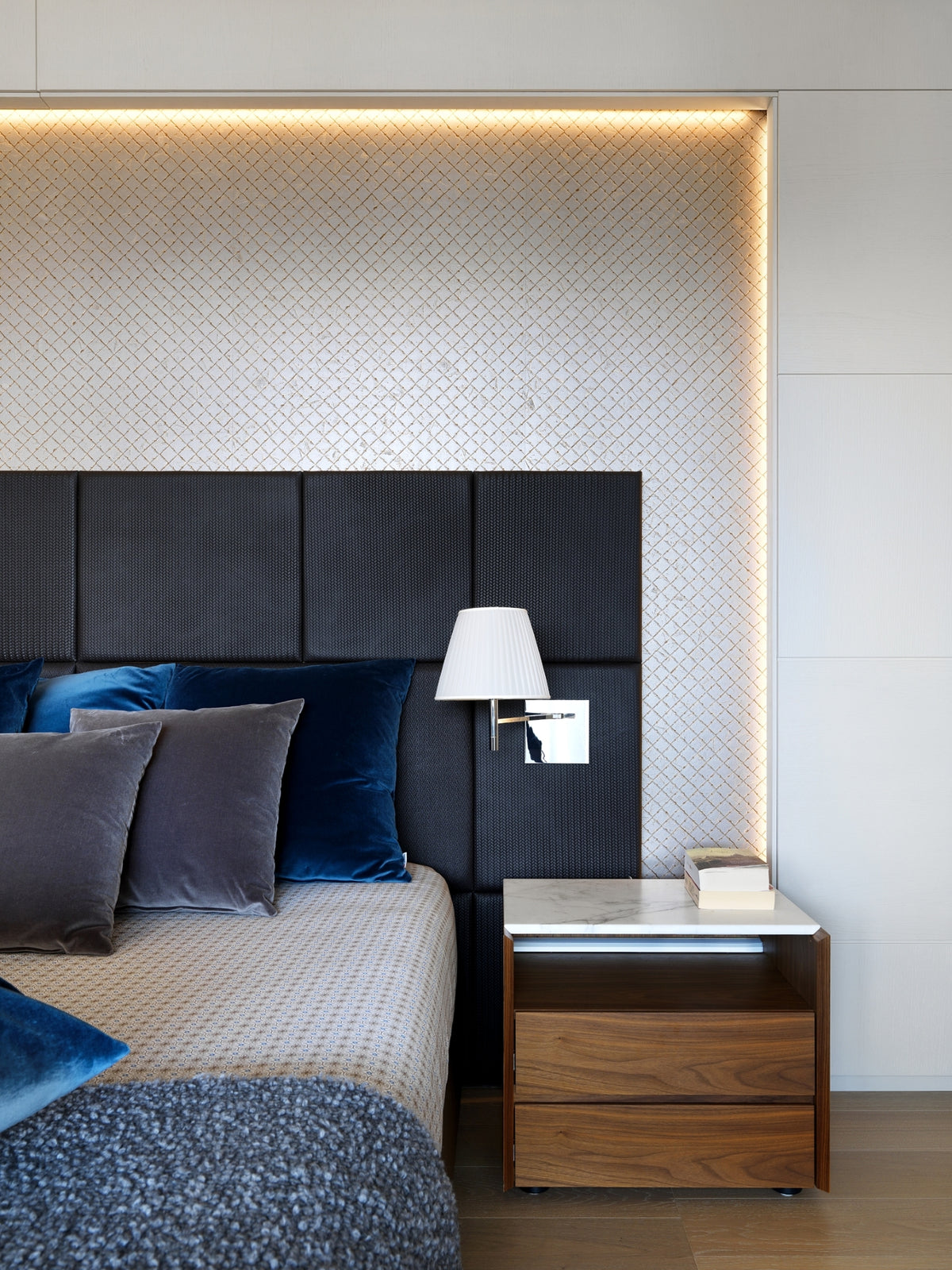 Letto matrimoniale con testata a boiserie tessile, con applique decorativa, comodino in legno e marmo, in nicchia illuminata