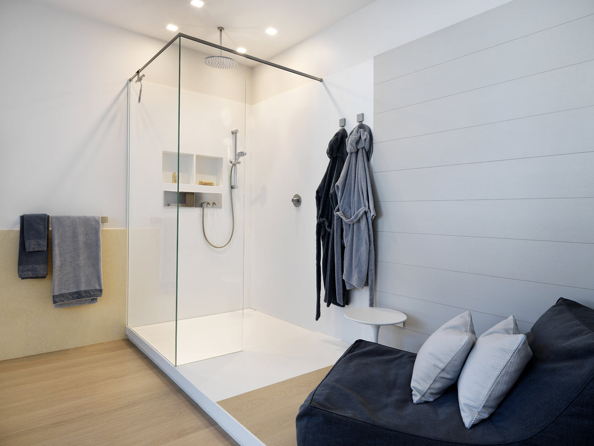 Bagno moderno con doccia walk-in, rivestimenti chiari e angolo relax con poltrona imbottita