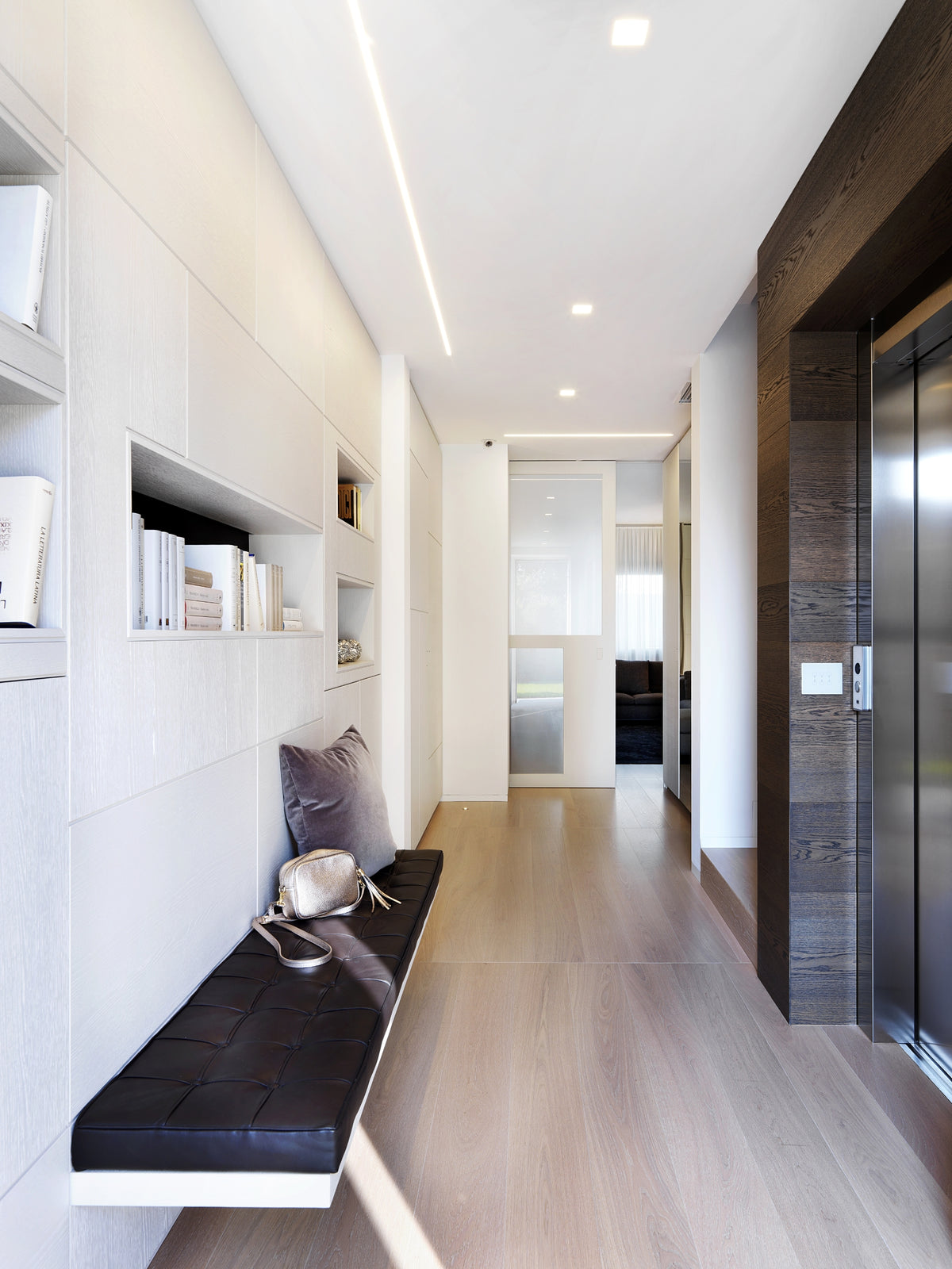 Ingresso con panca in pelle, boiserie attrezzata con nicchie decorative, ascensore e porte scorrevoli su misura