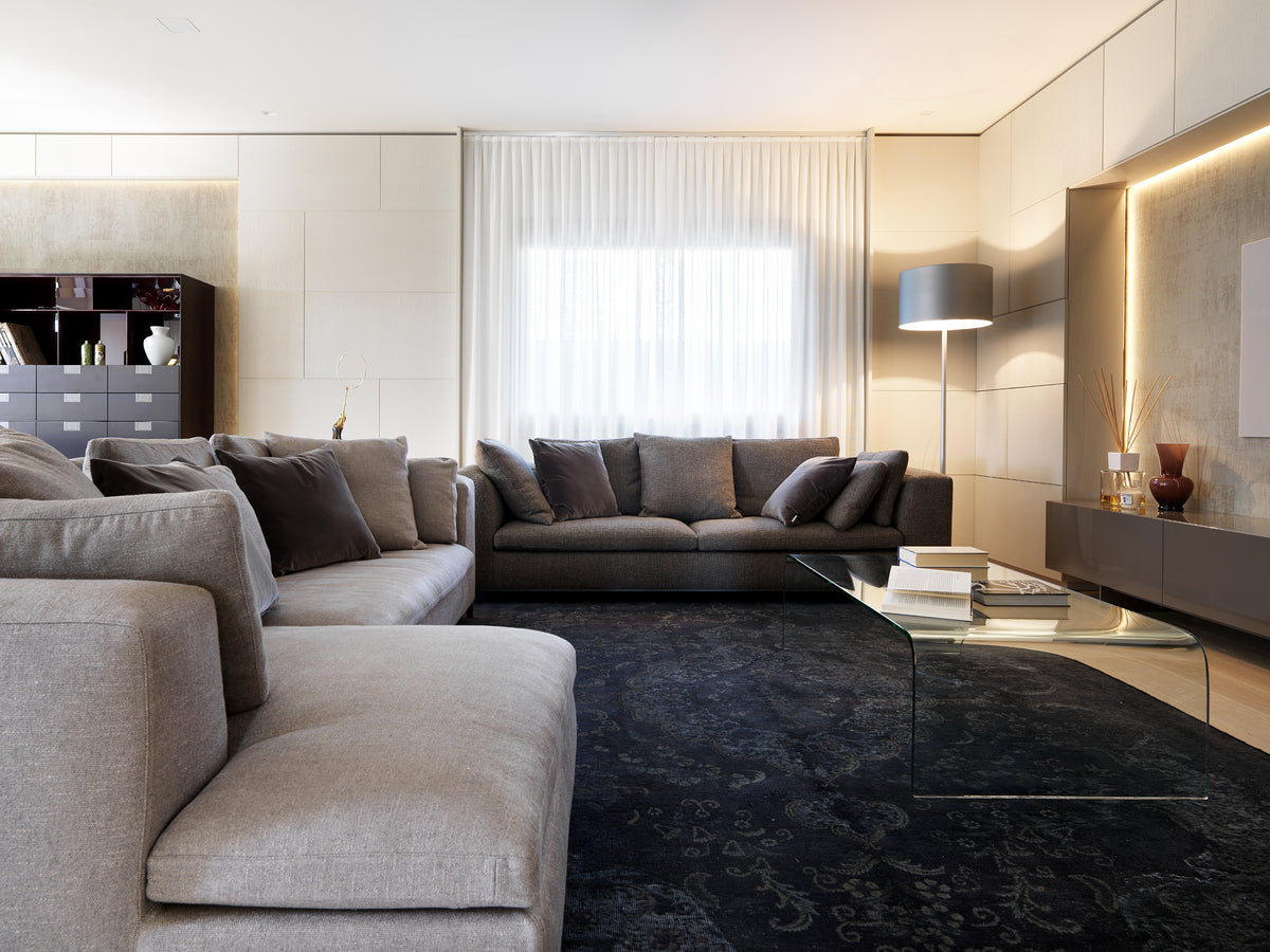 Soggiorno con composizione di divani modulari, tavolino in vetro curvato e pannellature decorative a parete con illuminazione indiretta