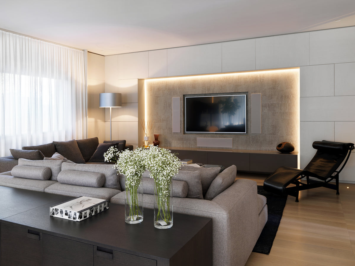 Zona living con doppio divano modulare, chaise longue e nicchia retroilluminata con parete TV e carta da parati materica