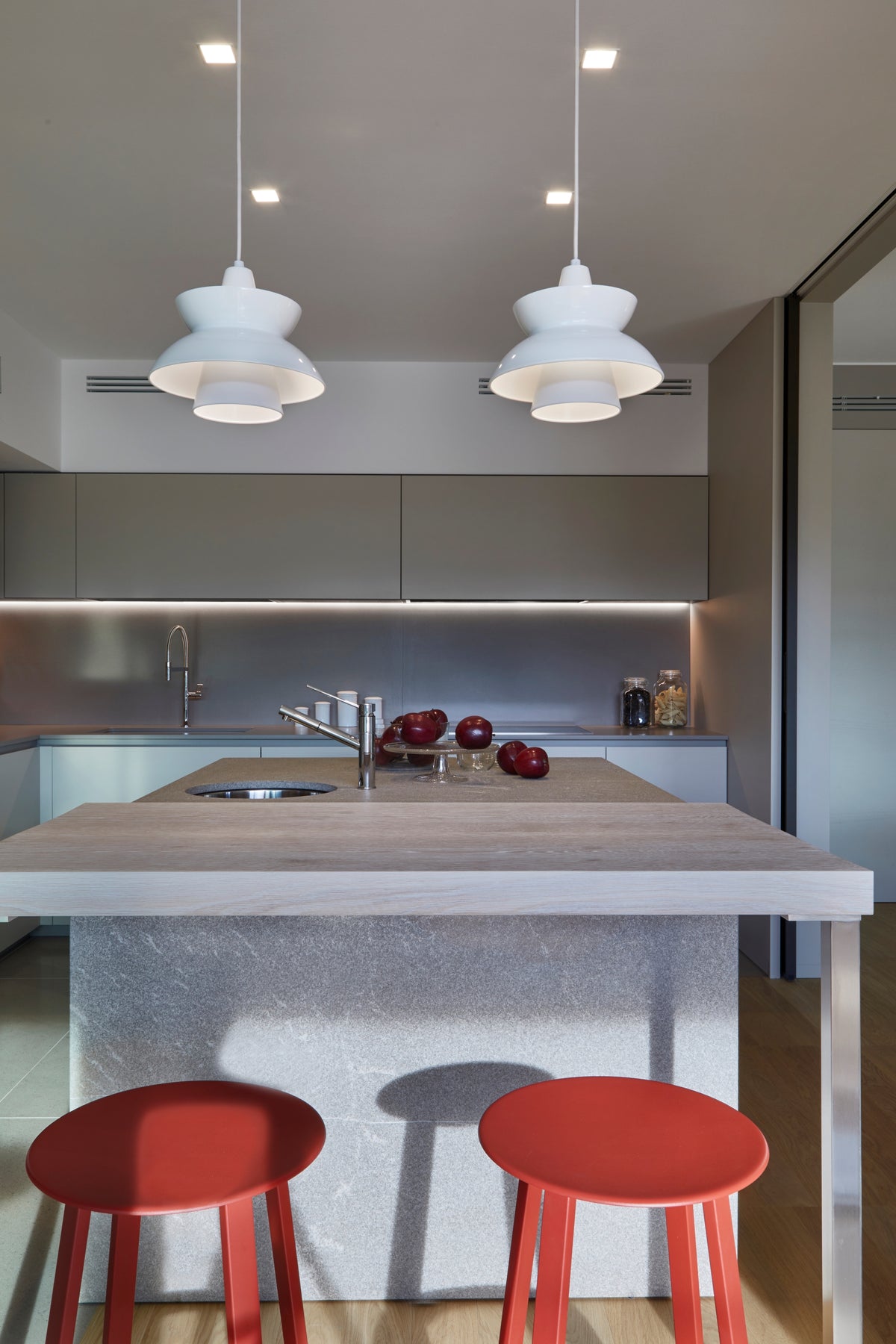 Dettaglio dell’isola cucina con piano snack in legno, sgabelli rossi a contrasto e lampade a sospensione di design