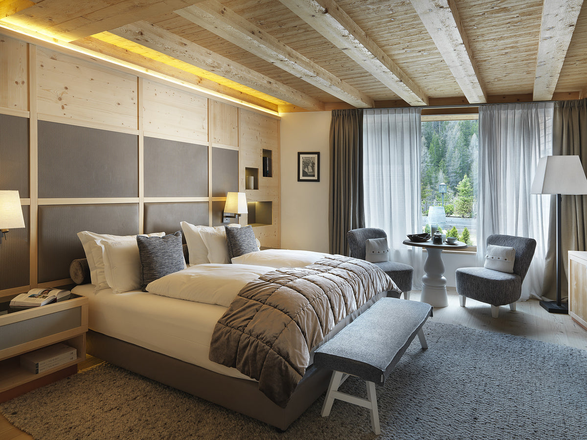 Camera matrimoniale dalla calda atmosfera alpina, con boiserie su disegno e area relax in una suite privata di hotel 5 stelle