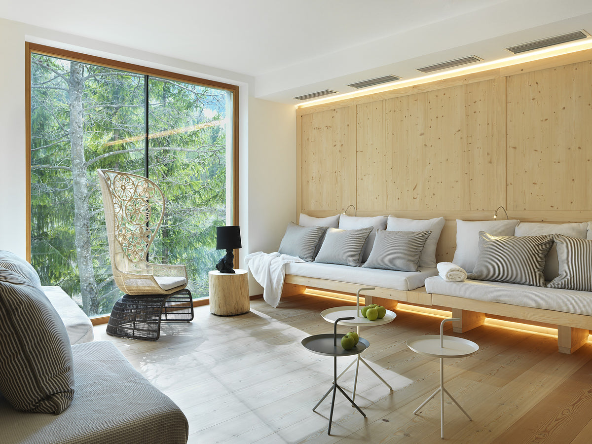 Zona relax con grande finestra, divano lineare e luce naturale a contatto con il bosco
