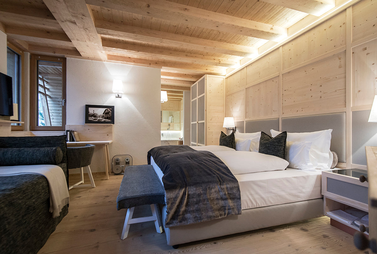 Camera di hotel 5 stelle con letto in pelle, panca imbottita e boiserie in legno e tessile sotto travi a vista