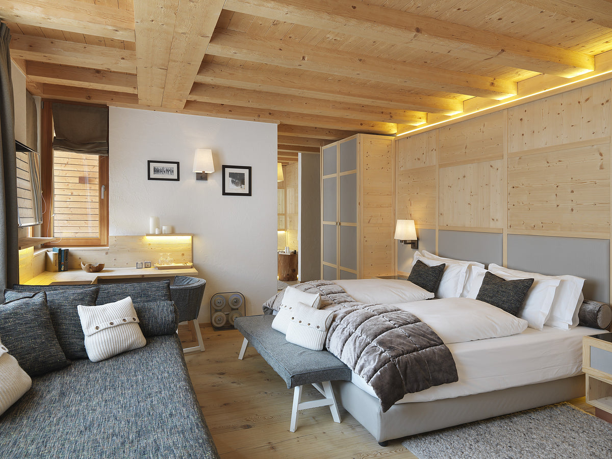 Camera con letto matrimoniale, area lounge e scrivania, con arredi integrati in legno chiaro