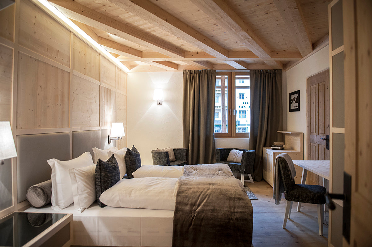Camera da letto con testata tessile e boiserie in legno, travi a vista e angolo scrittoio