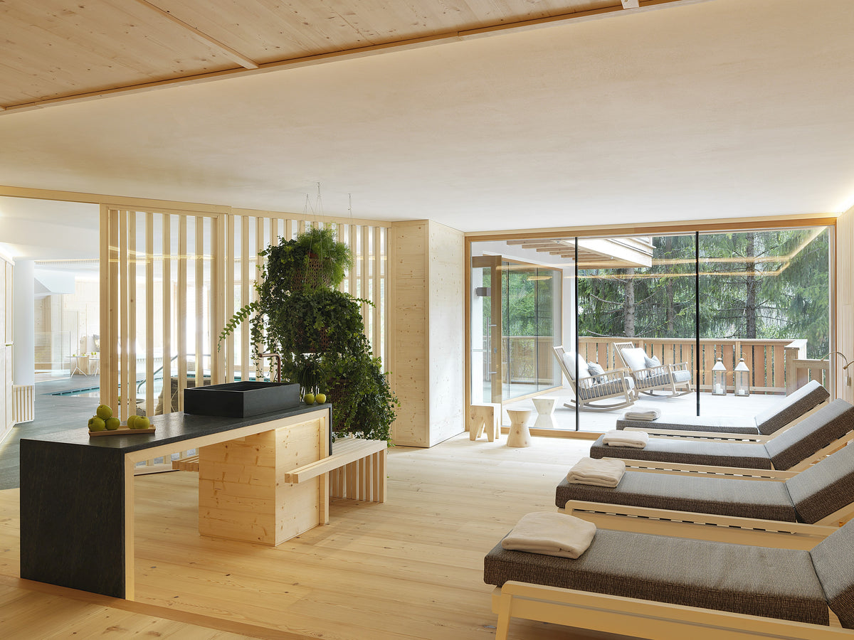 Spazio relax wellness con lettini imbottiti in tessuto, vista sull’esterno con poltrone a dondolo e arredi coordinati in legno chiaro