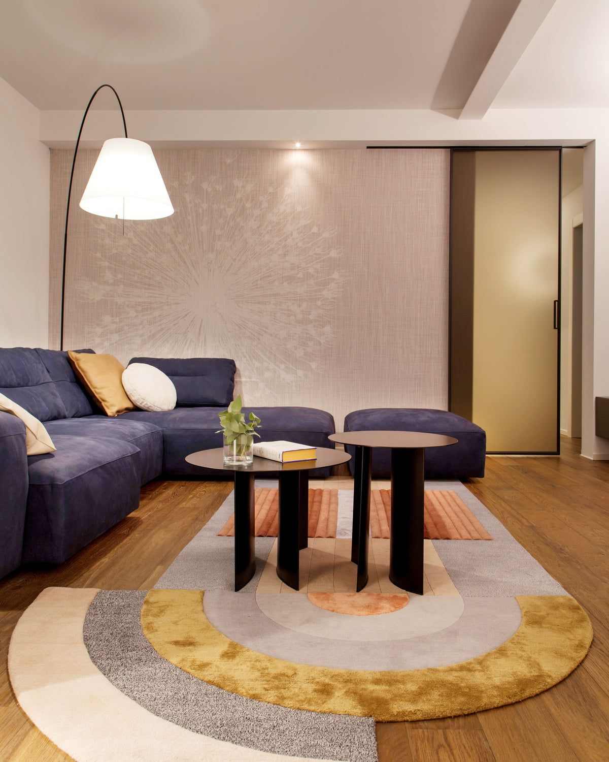 Dettaglio della zona relax con divano angolare blu, tavolini neri e tappeto colorato di design con forma irregolare