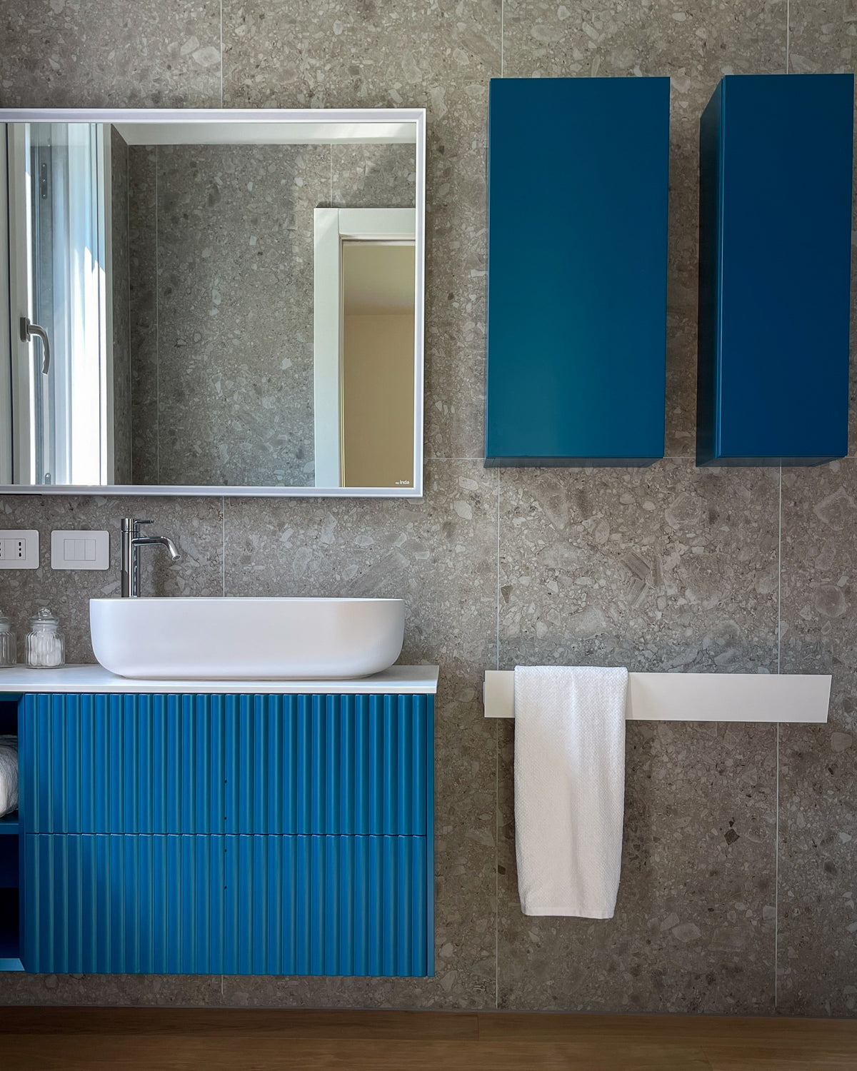 Dettaglio del bagno su misura con mobile blu ottanio, lavabo da appoggio e rivestimento materico effetto ceppo di gré