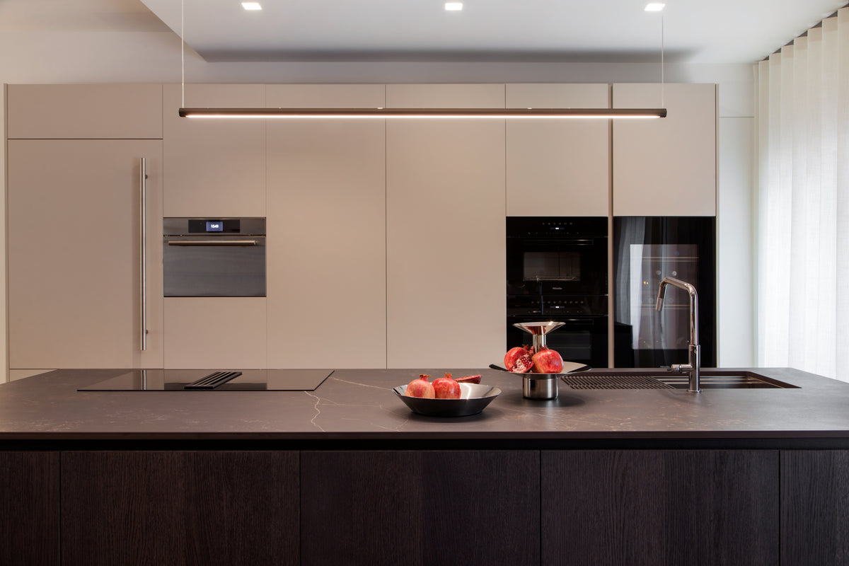 Parete cucina con colonne attrezzate, elettrodomestici integrati e grande isola con lavello e piano cottura a induzione con aspirazione integrata