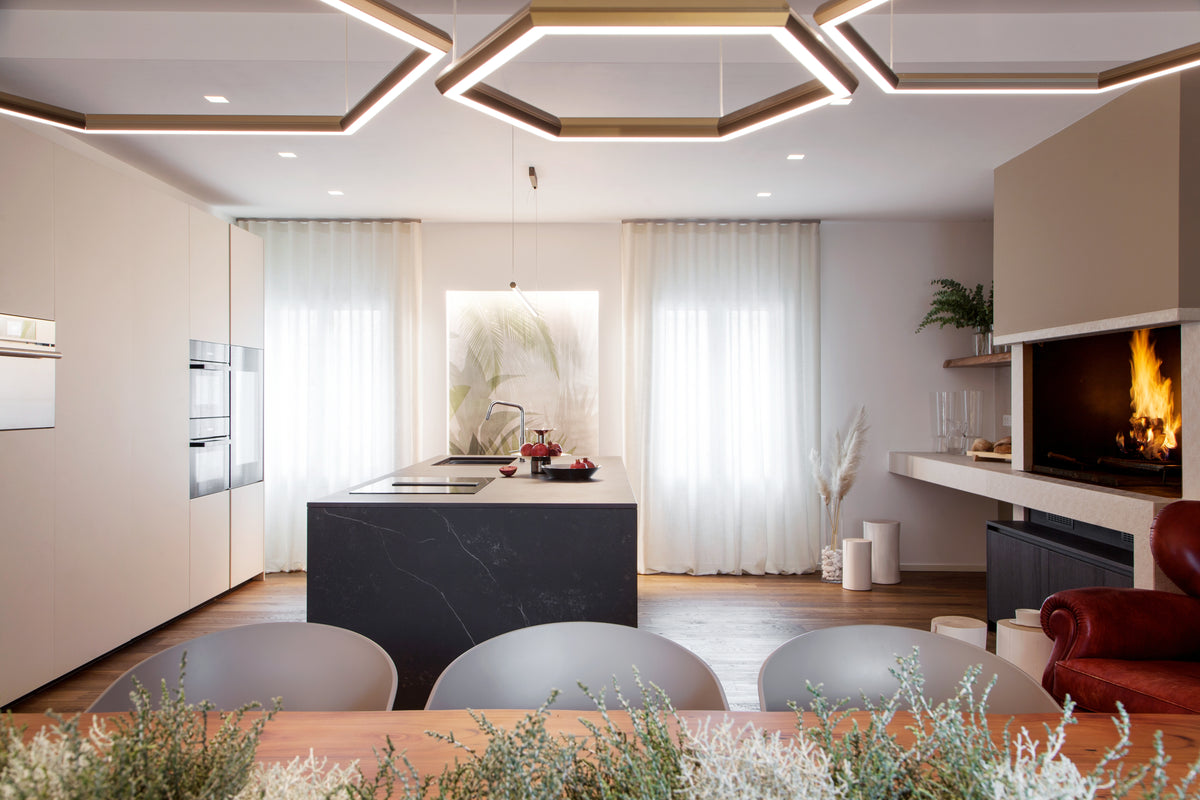 Zona giorno con cucina a isola, tavolo da pranzo, camino e lampade geometriche in un progetto residenziale dal gusto contemporaneo