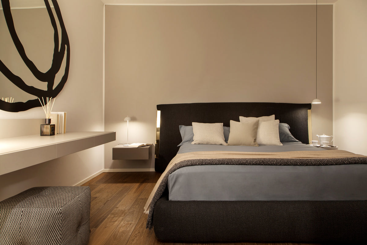 Camera matrimoniale con letto tessile scuro, comodini sospesi e illuminazione discreta in un interno elegante e contemporaneo