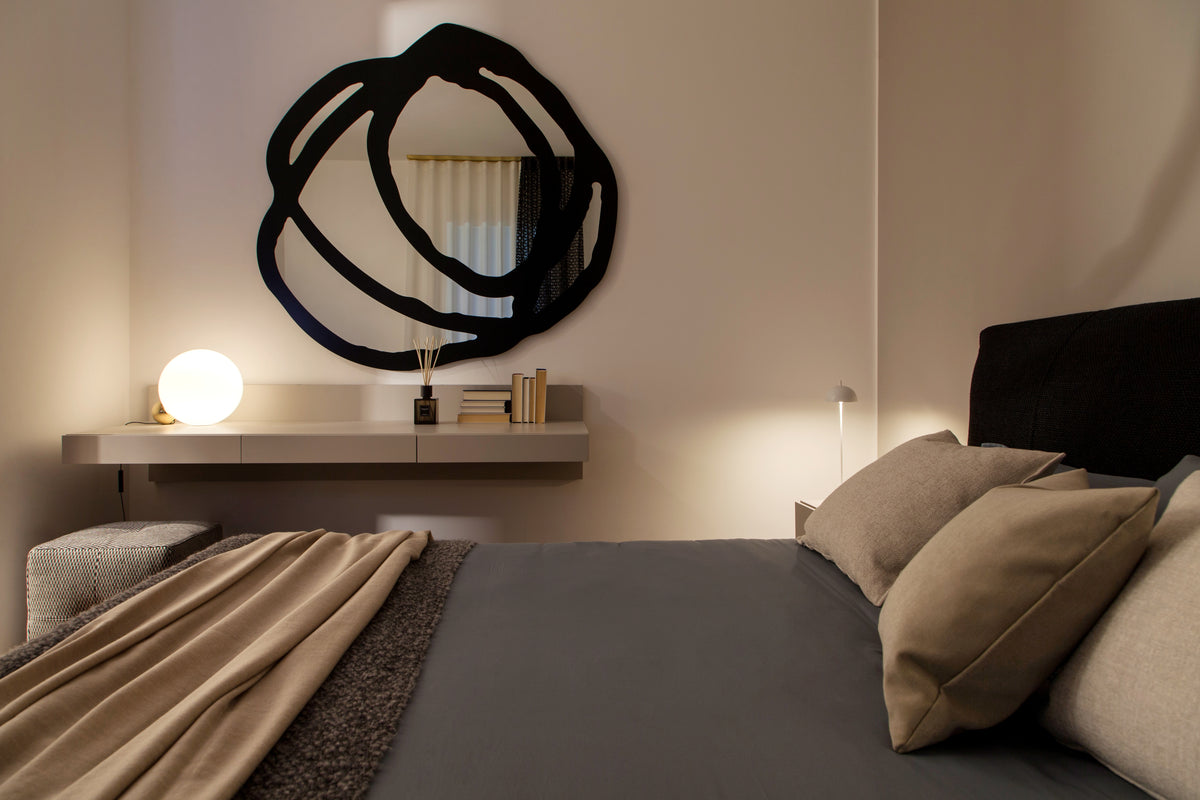Camera da letto con specchio decorativo, console sospesa dal disegno essenziale e lampada da appoggio di design a sfera