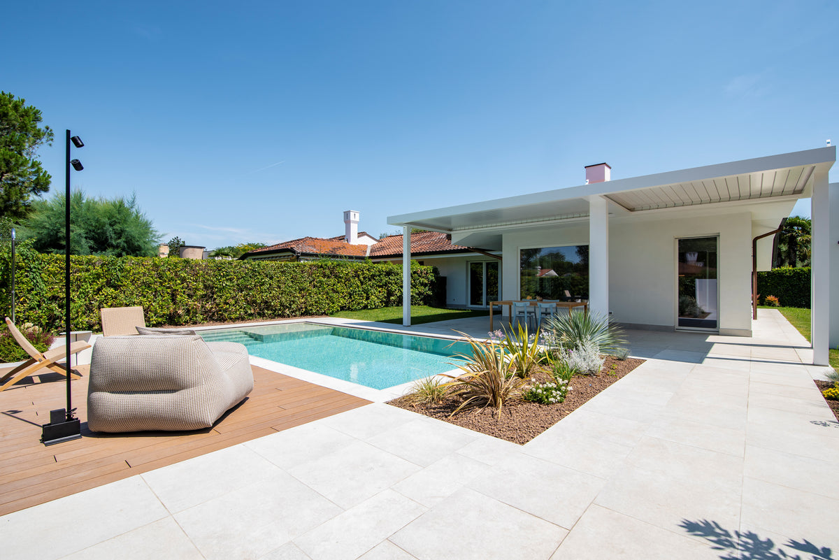 Piscina con area lounge, portico e giardino progettati in continuità con l’abitazione